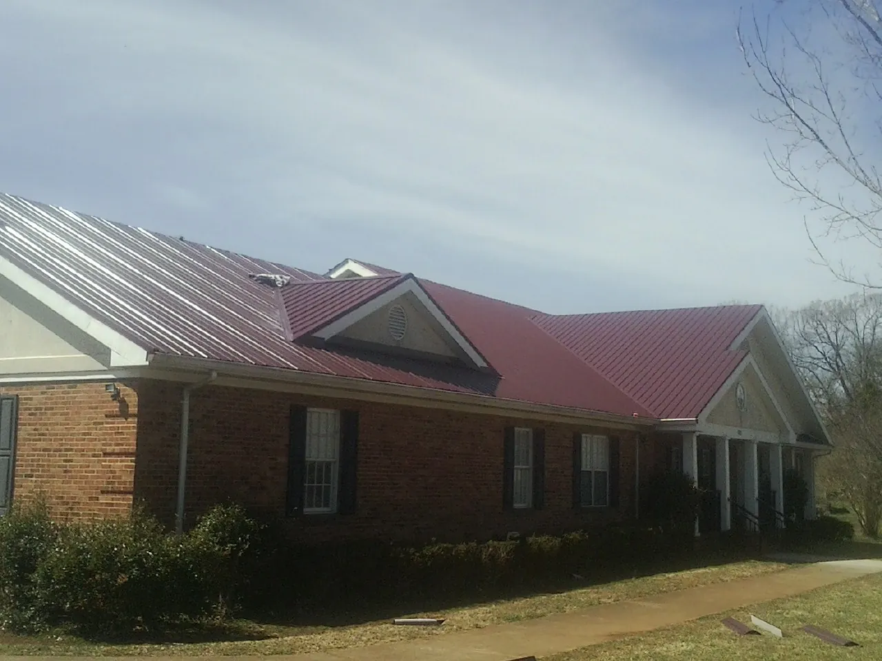 Red metal roof with gabled entries on a long brick building, from a Hail Damage Roof Repair job in Skykomish
