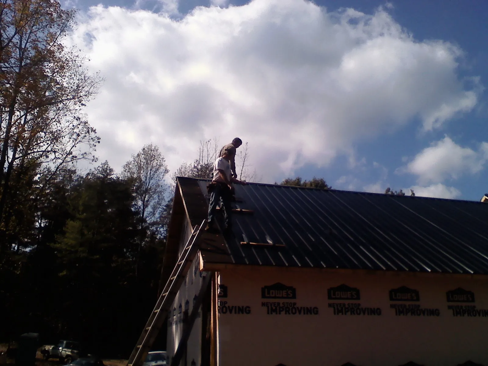Roofer fastening dark metal panels high against a cloudy sky, from a Roof Inspection job in Skykomish