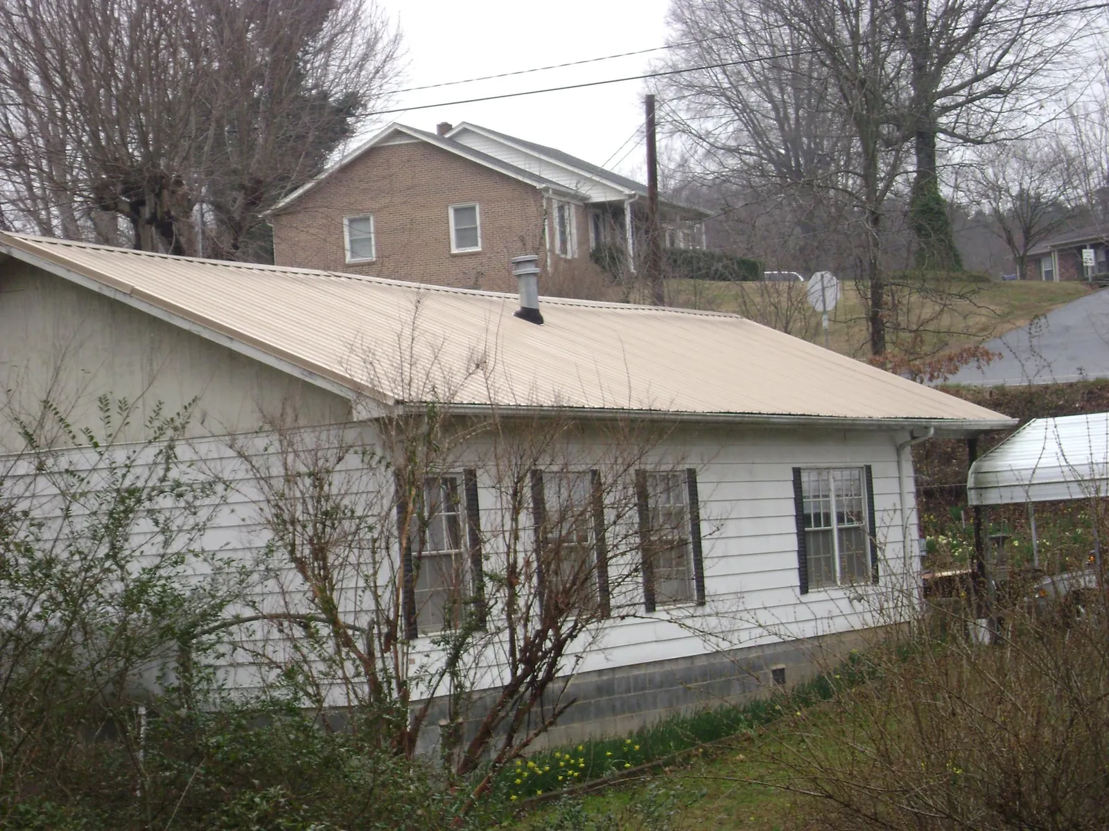 Tan metal roof on a white sided house set into a hillside — Commercial Roofing by Roofing Brothers in Skykomish